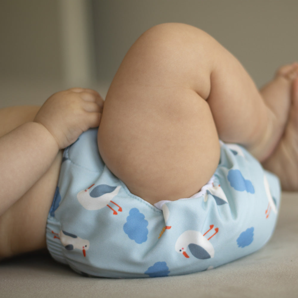 Baby auf dem Rücken liegend mit angezogenen Beinen, trägt die Little Clouds SuperCloud All-in-One-Windel im Design Möwen – zeigt die schmale Passform