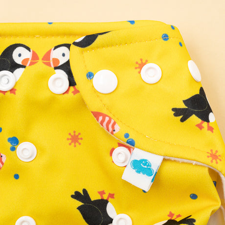 Nahaufnahme der Little Clouds Prefold-Überhose aus PUL im Design Papageientaucher mit Druckknöpfen und blauem Etikett