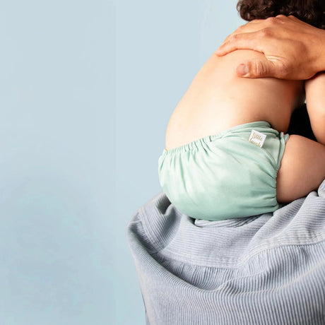 Baby auf dem Arm eines Erwachsenen trägt eine mintgrüne Little Lamb Pocketwindel, Ansicht von hinten