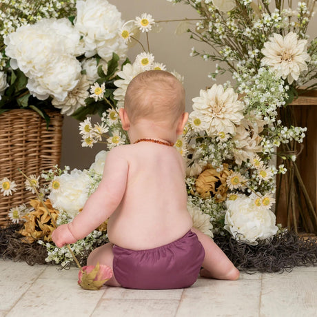 Baby sitzt zwischen Blumen und trägt die Little Lamb Pocketwindel in Aubergine, Ansicht von hinten